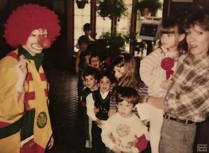 Children and adults posing with a clown in an awkward family photo that somehow feels incredibly sweet and nostalgic.