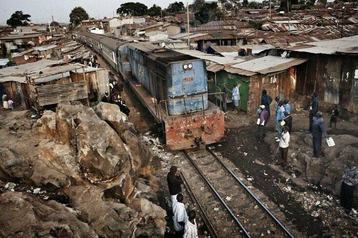 Train navigating through crowded slum area, depicting urban hell reality.