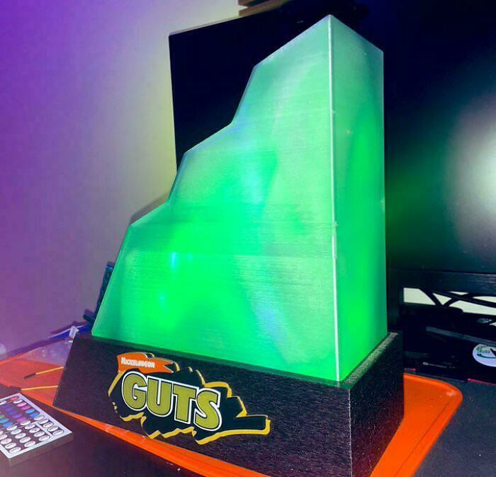 Nickelodeon GUTS trophy with a glowing green rock wall, symbolizing the wild ’90s nostalgia.