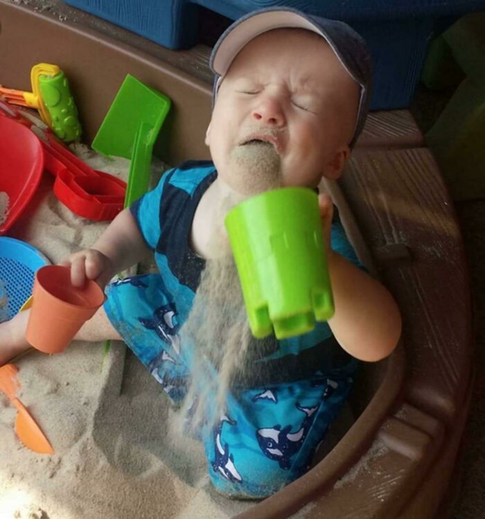 A child unintentionally pouring sand over themselves in a sandbox, illustrating a humorous moment of being clueless.