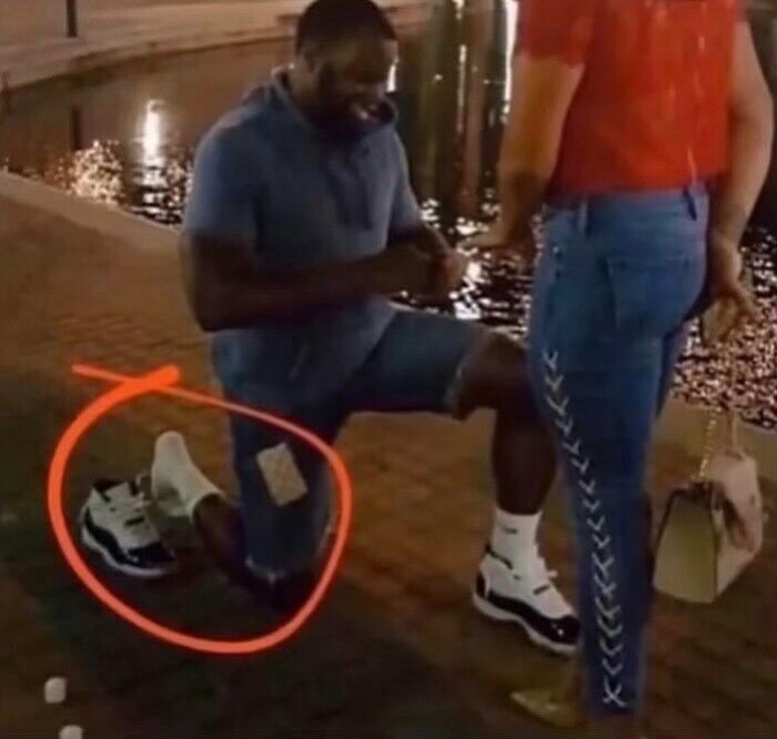 Man kneeling by water wearing socks with sandals and ripped jeans, showcasing a weird side of the internet moment.