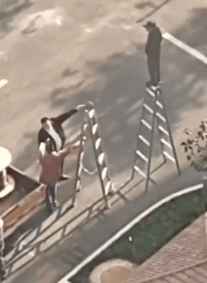 Confusing perspective of a person on a ladder creating an optical illusion with another person on the ground.