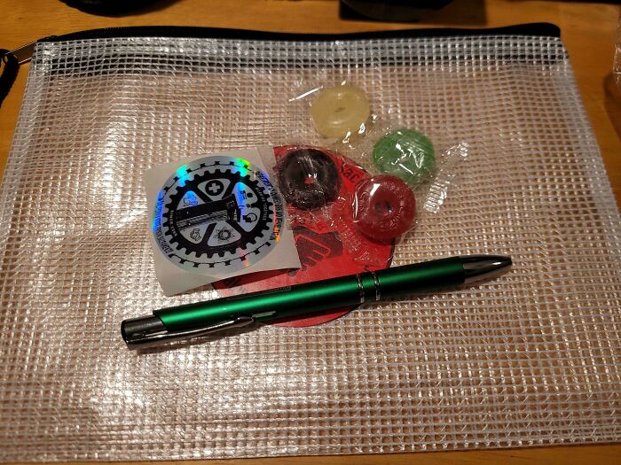 Gift bag containing a green pen, three candies, and a sticker, illustrating infuriating company gifts and bonuses.
