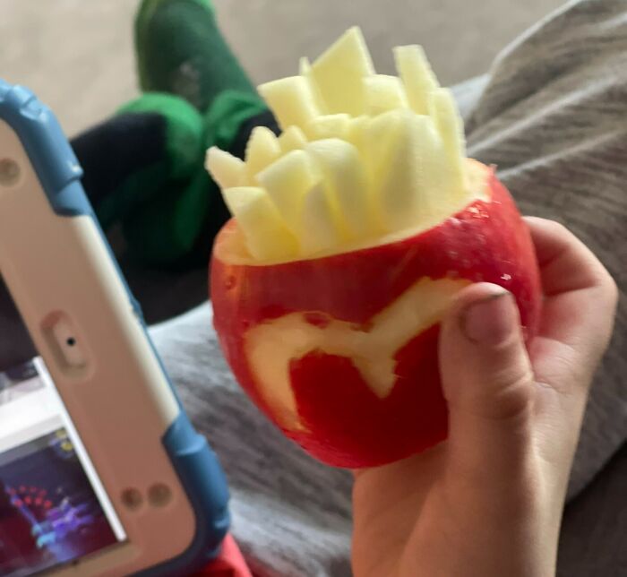 A child holding an apple carved to look like a cup of fries, depicting dumb-clueless-kids' creativity.