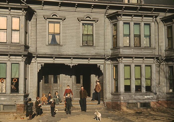Group of people and a dog outside a large house, depicting life in 1940 color photos.