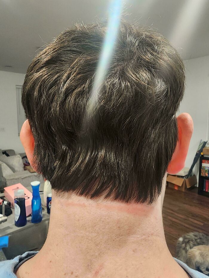 The back of a man's head shows a very short, unfortunate haircut with a harsh line at the neck.