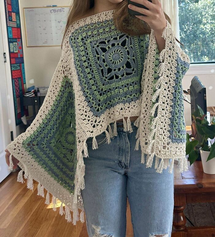Crochet enthusiast wearing a handmade green and cream crocheted poncho with tassels, proudly showing off the project.