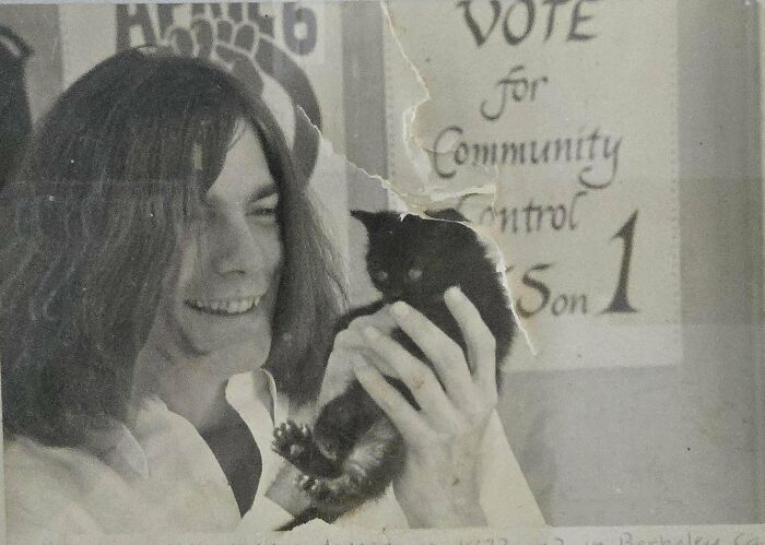 Young person with long hair holding a black cat smiling in a vintage photo from fascinating old images history collection