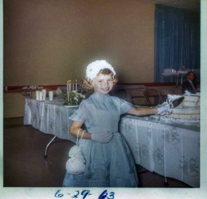 Young girl in vintage dress and bonnet smiling by a decorated table with cake in a fascinating old image from 1963.