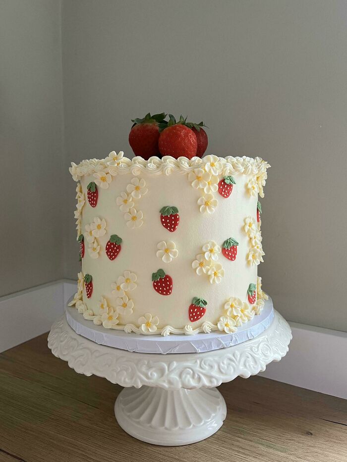 A beautifully decorated cake with strawberries and flowers, showcasing a baker's culinary creativity.