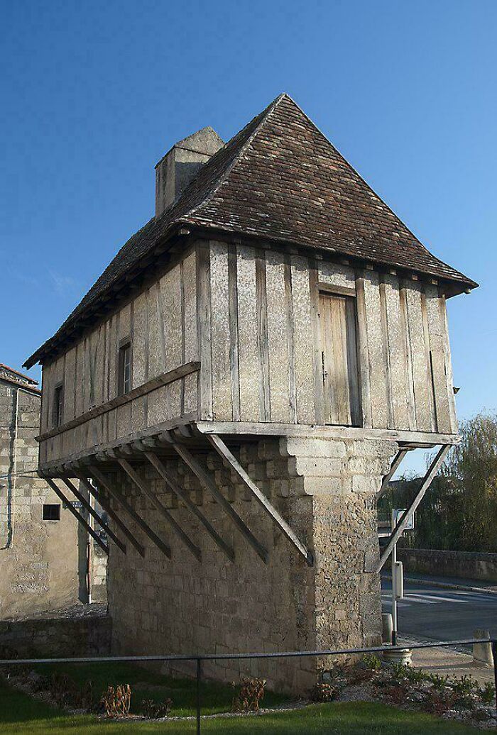 Unique bizarre building with a stone base and wooden upper structure, supported by angled beams against a clear blue sky.