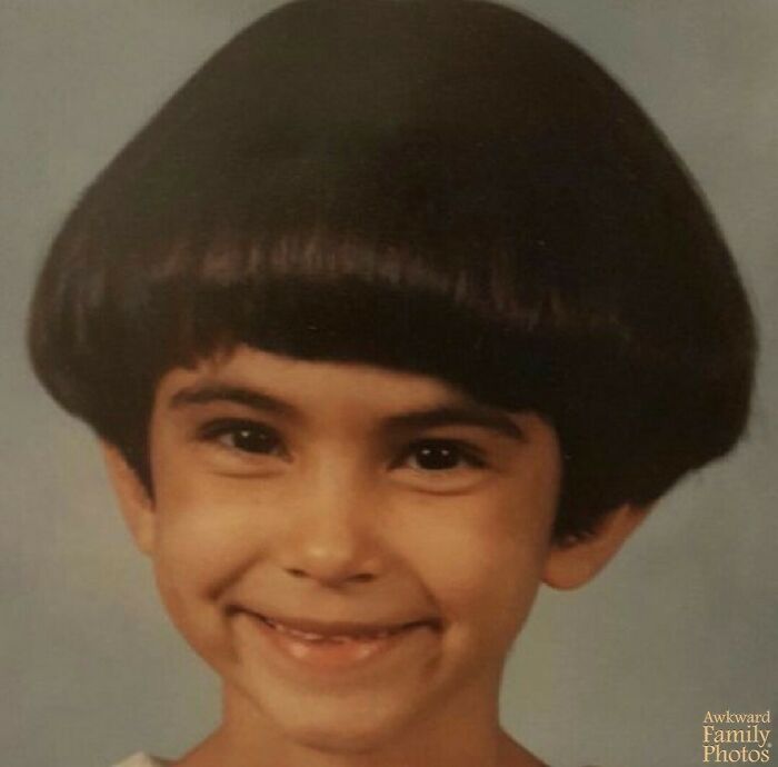 Child with a vintage bowl haircut smiling in an awkward family photo that feels both funny and sweet.