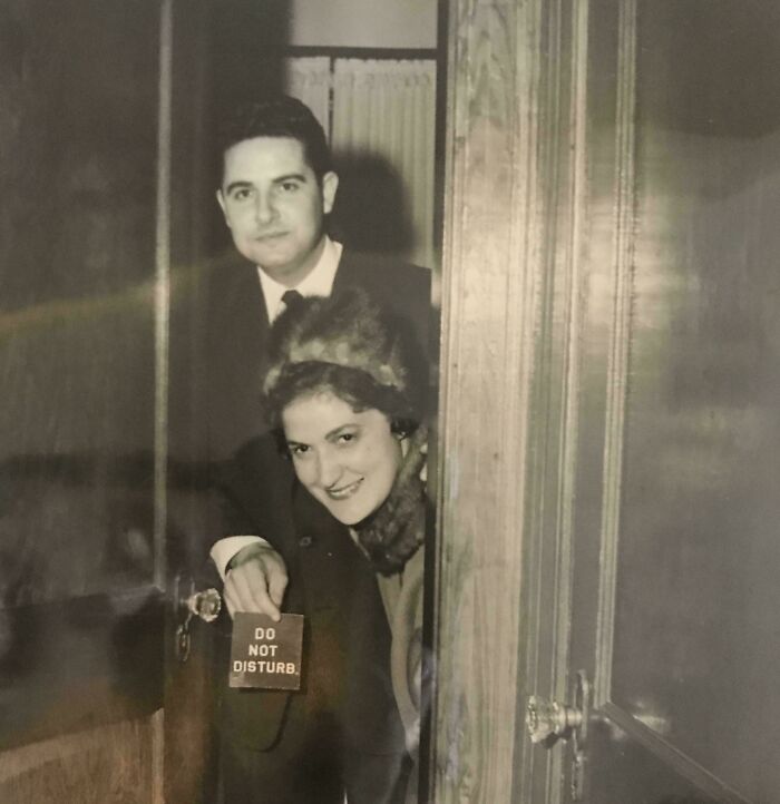 Couple posing behind a door holding a do not disturb sign in a fascinating old image likely unseen in history class.