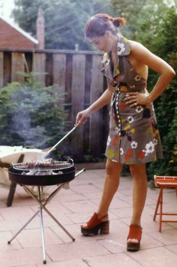 Woman in vintage dress grilling outside on a patio, a fascinating old image from history class archives.