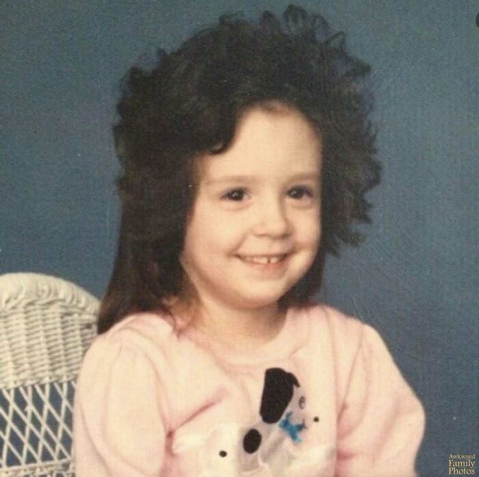 Young girl with a big curly hairstyle wearing a pink sweater in an awkward family photo that feels incredibly sweet.