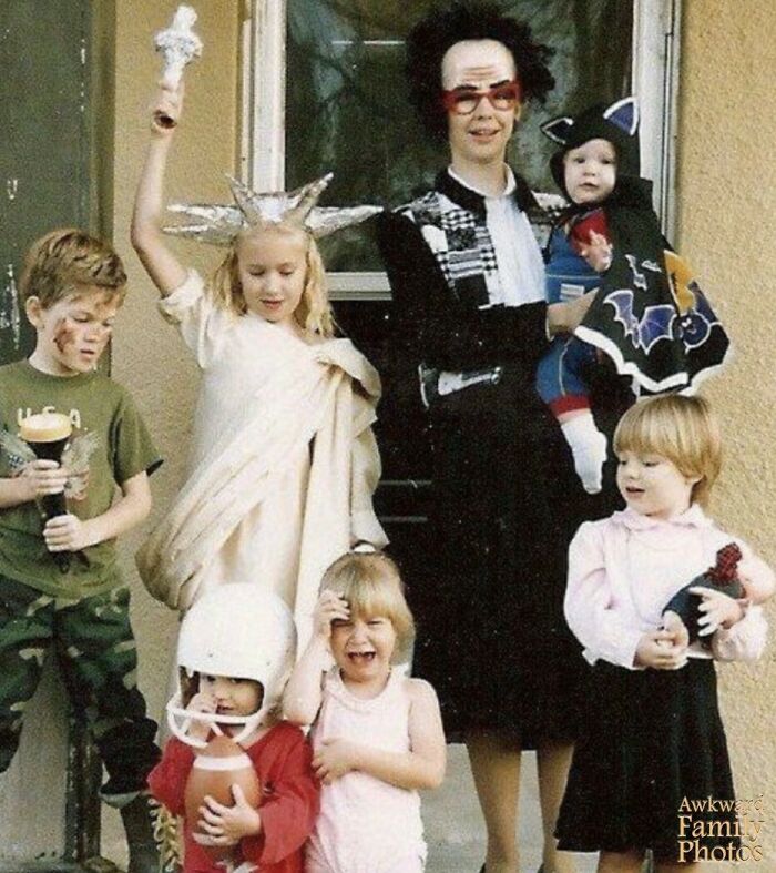A quirky family dressed in mismatched costumes posing awkwardly for a sweet family photo outside their home.