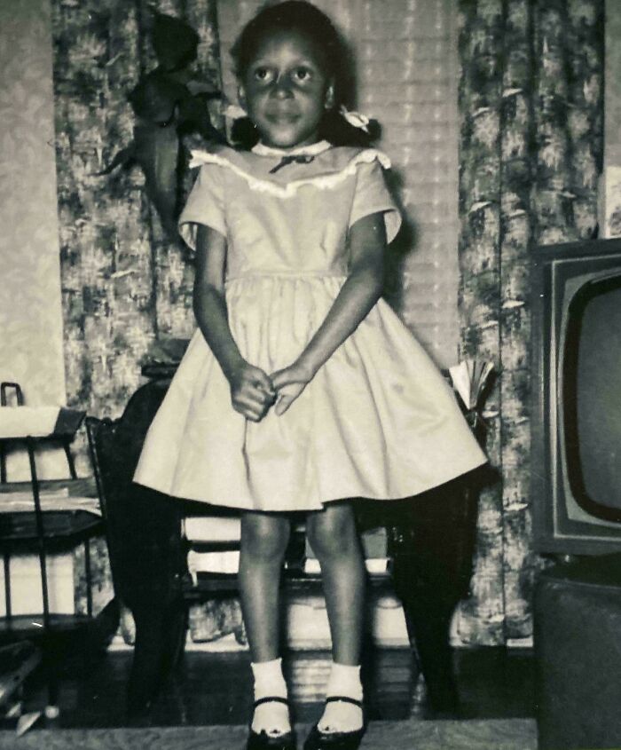 Young girl in a vintage dress standing in a living room, one of the fascinating old images rarely seen in history class.