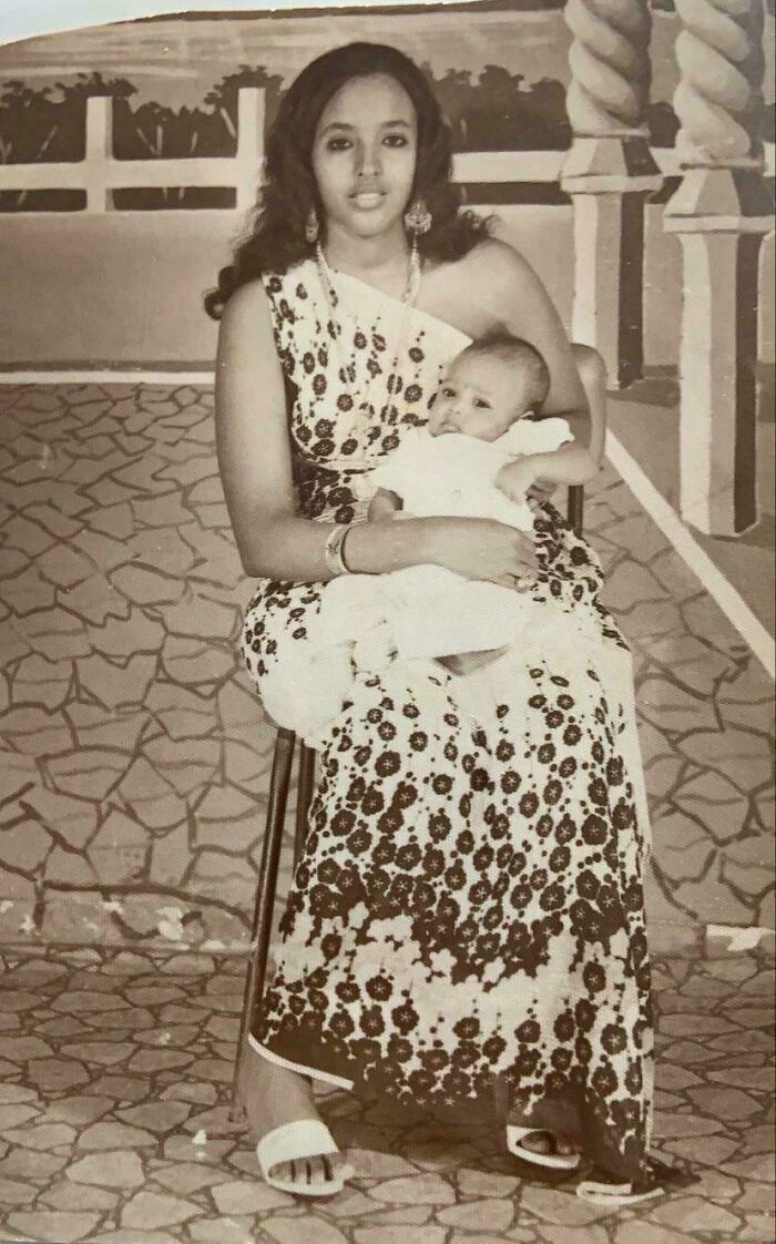 Young woman holding a baby, dressed in traditional attire, captured in a fascinating old image from history.