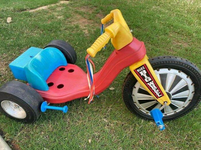 Red and yellow vintage Big Wheel tricycle with blue seat and pedals on grass, a nostalgic photo of childhood toys.