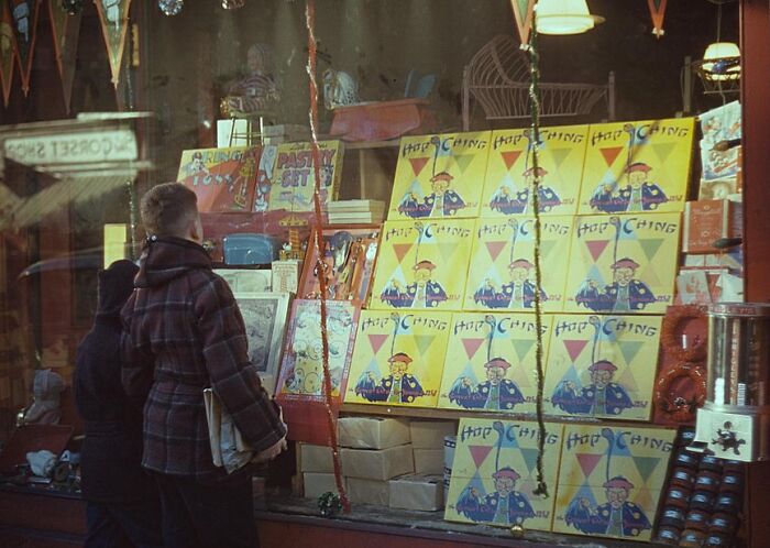 Two people viewing a vibrant 1940s shop window display with colorful magazines and toys.