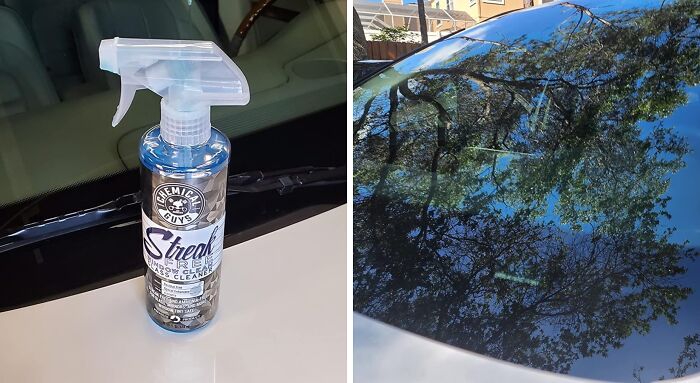Spray bottle of car window cleaner next to a clean and shiny car windshield, reflecting trees overhead.