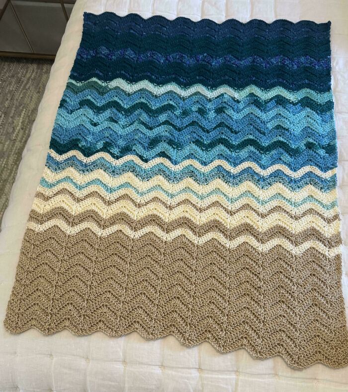 Crochet blanket with wavy stripes in shades of blue, cream, and beige showcasing crochet masterpieces.