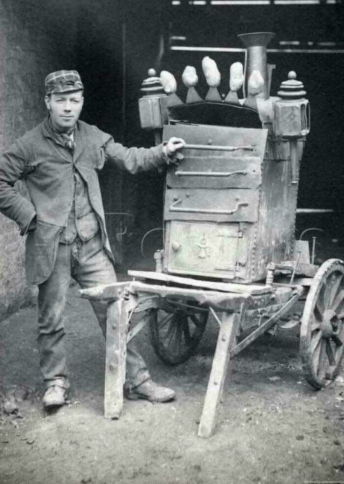 Man standing next to a vintage mobile furnace, an old image showing fascinating history equipment and technology.