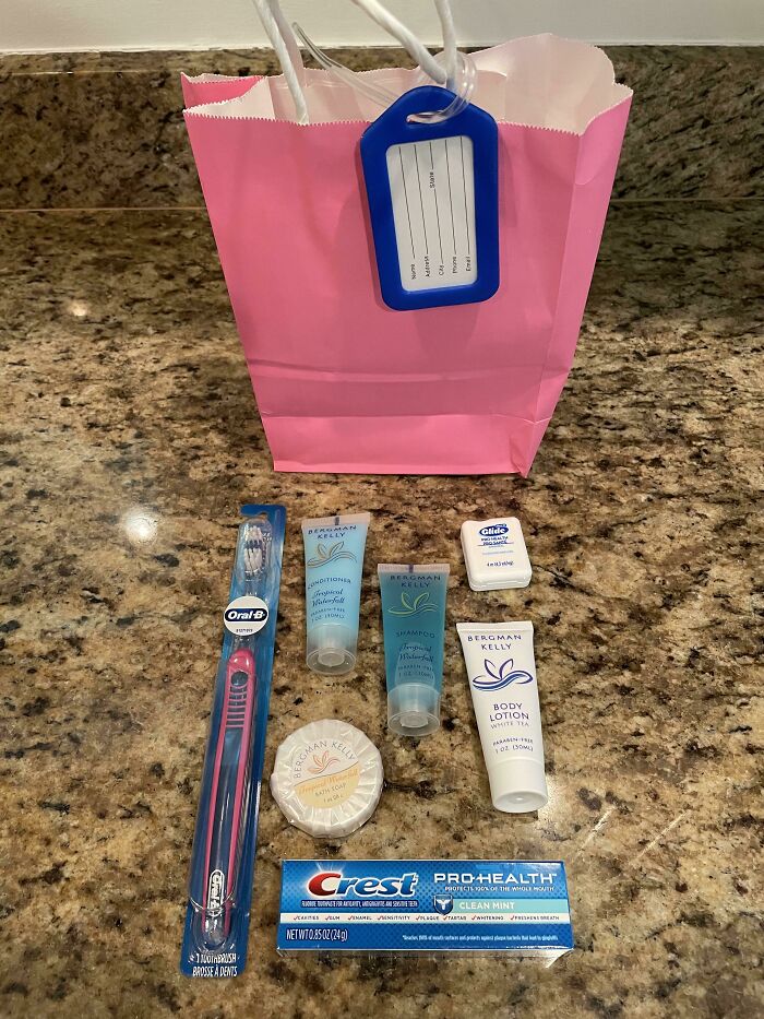 Pink gift bag with toiletries, including a toothbrush, toothpaste, lotion, and soap, as company gifts or bonuses.