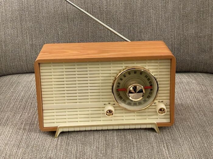 Vintage retro radio with tuning dial and antenna, sitting on a textured grey fabric surface, evoking nostalgic old soul vibes.
