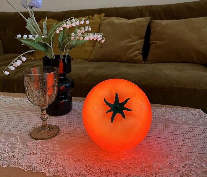 Retro fever: A glowing tomato lamp on a lace-covered table beside a vintage glass and flower arrangement.