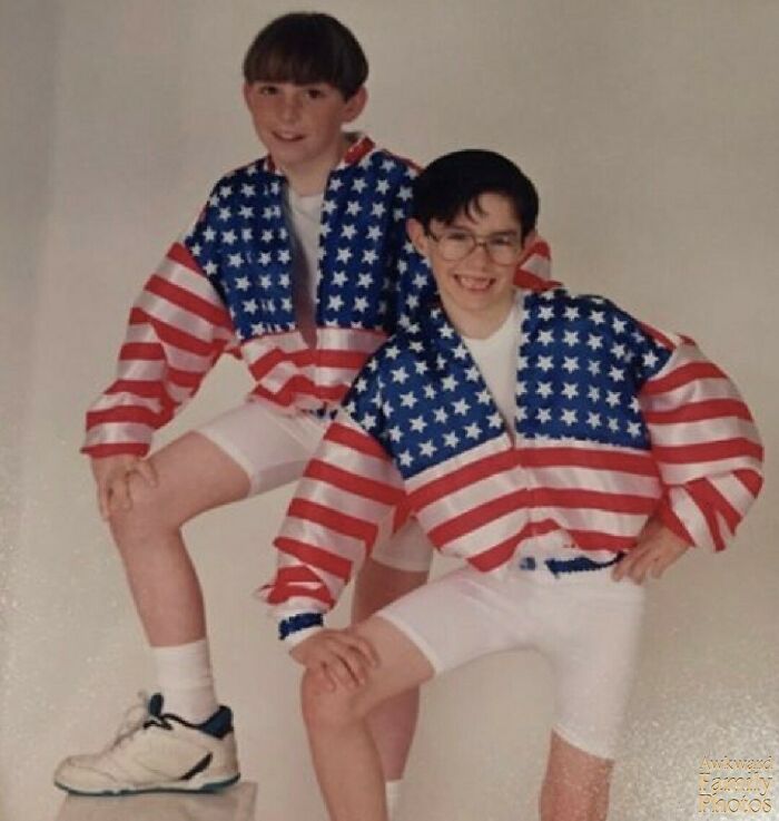 Two boys in matching American flag jackets and white shorts posing for an awkward family photo with sweet smiles.