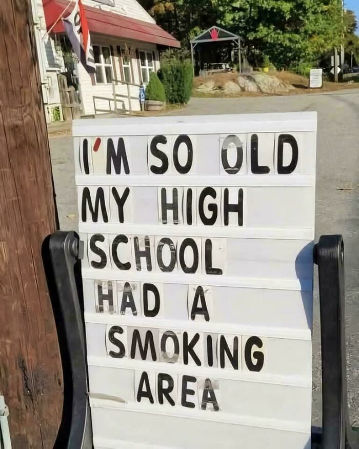 Sign reads "I'm so old my high school had a smoking area," reminiscing childhood past in front of a rural building.