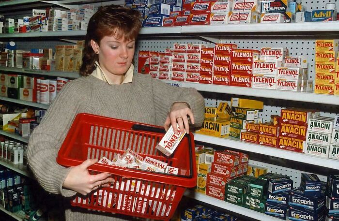 A woman in a sweater shopping for Tylenol in a retro pharmacy, evoking childhood memories.