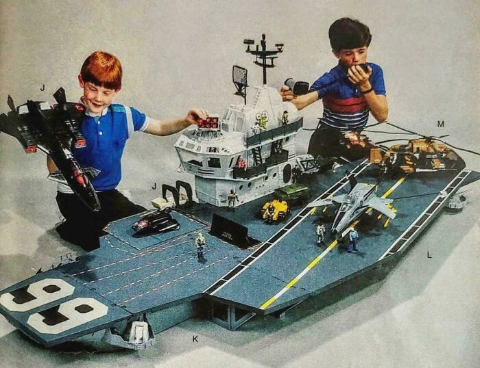Young boys playing with a large aircraft carrier toy set, evoking childhood memories.