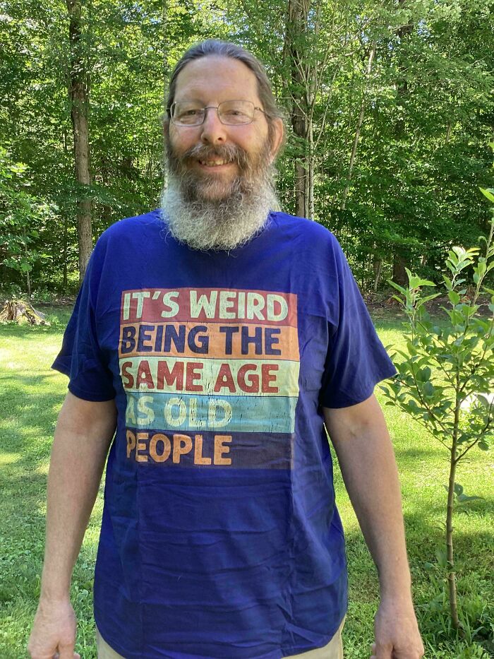 Man wearing a humorous shirt about aging, standing outdoors, evoking childhood nostalgia.