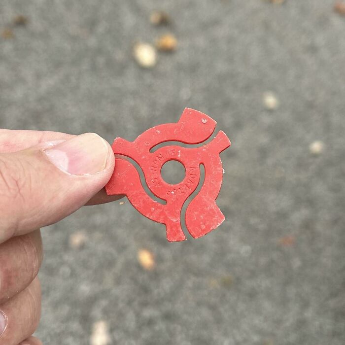 Red plastic adapter for 45 RPM records held between fingers, invoking childhood memories.