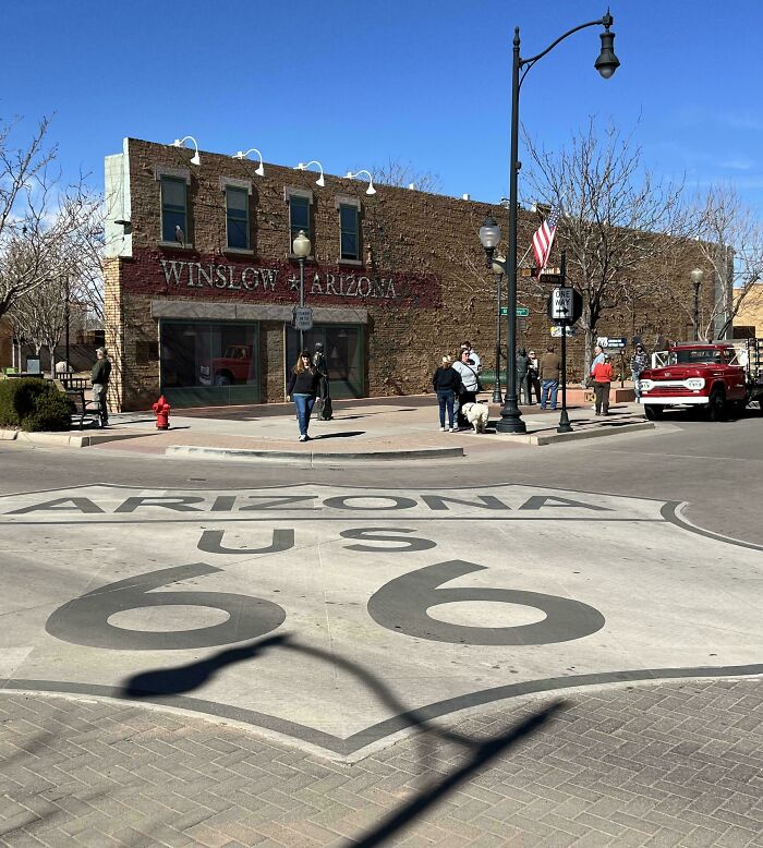 Winslow, Arizona Route 66 sign with people and a vintage truck nearby, evoking nostalgic childhood memories.