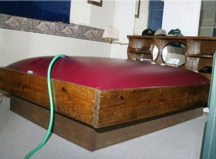 Childhood reminder: A retro waterbed filling with water in a bedroom, featuring wood frame and mirror in the background.