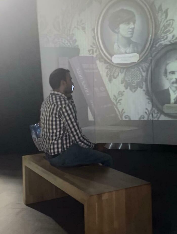 Person sitting on a bench blocking projector screen, displaying historical photos, in a dimly lit room.
