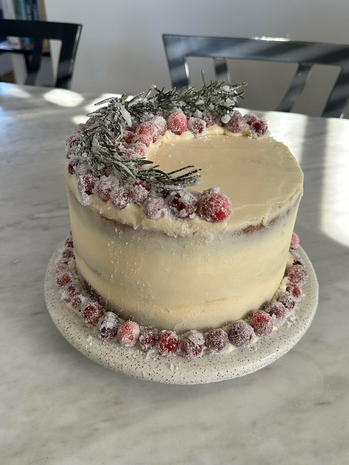 Beautifully decorated cake with sugared cranberries and rosemary, showcasing a baker's culinary concoctions.