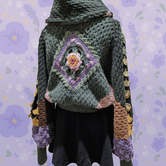 Crochet masterpiece hoodie with floral pattern in green, purple, pink, and yellow yarn displayed on a mannequin.