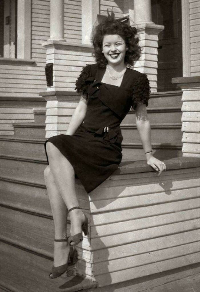 Vintage photo of a smiling woman in a black dress sitting on wooden porch steps in fascinating old images.