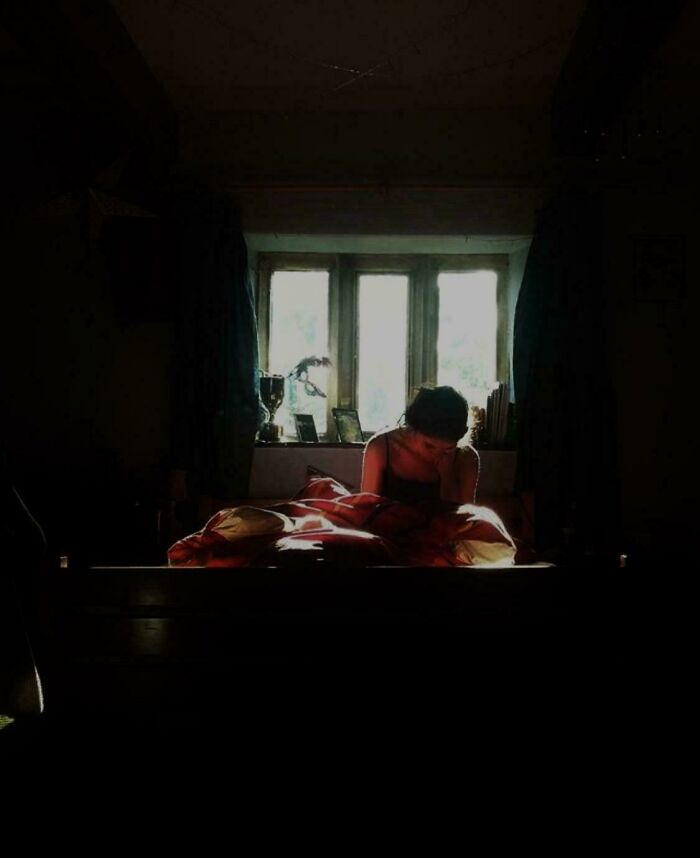 Woman reading by a window, illuminated by natural light, creating an accidental Renaissance painting effect.