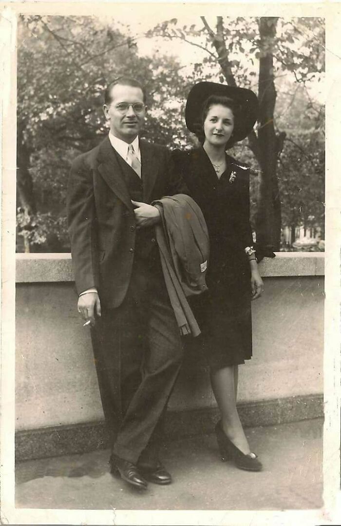 A couple in vintage attire, posing elegantly against a stone railing in a historical photograph.