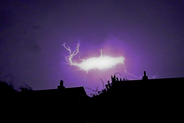 Purple lightning illuminating the night sky, showcasing a stunning natural phenomenon above silhouetted rooftops.