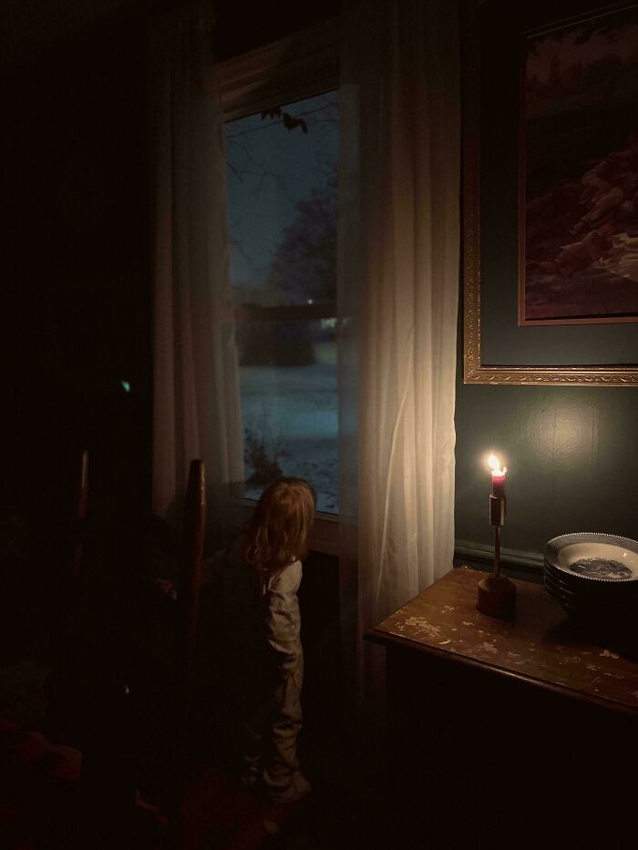 Child gazing out a window at night, dimly lit by a candle, evoking an accidental Renaissance painting atmosphere.