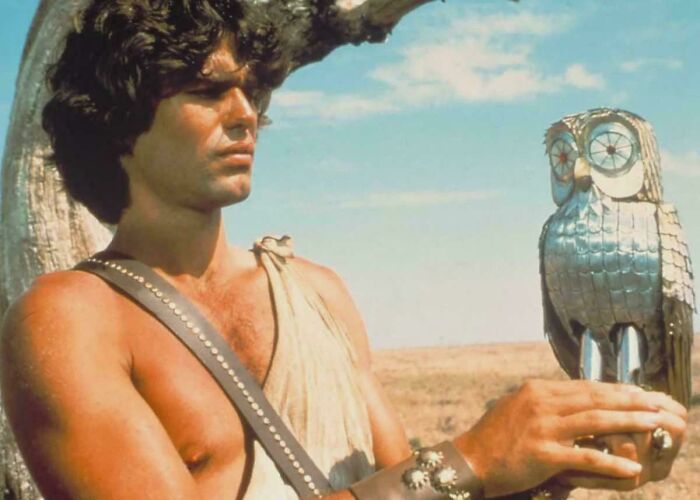 Man in ancient warrior costume holding a metallic owl statue in a nostalgic photo from past decades.