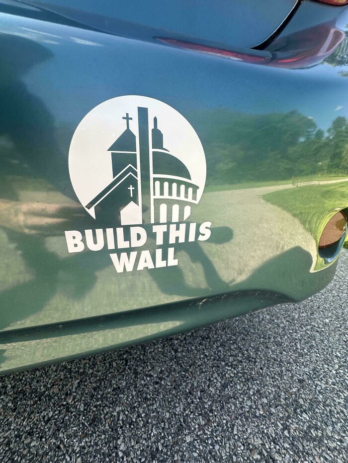 Car with funny bumper sticker reading "Build This Wall" featuring church and capitol building icons.