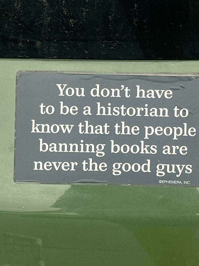 A funny bumper sticker about book banning on a green vehicle.
