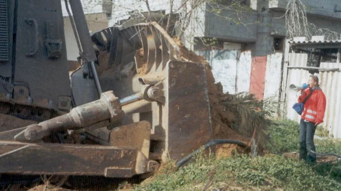 La activista estadounidense Rachel Corrie, de 23 años, entre una excavadora israelí y una casa palestina el 16 de marzo de 2003 en Rafah, Franja de Gaza. Corrie murió atropellada por una excavadora israelí cuando protestaba por la demolición de casas palestinas. (2003)
